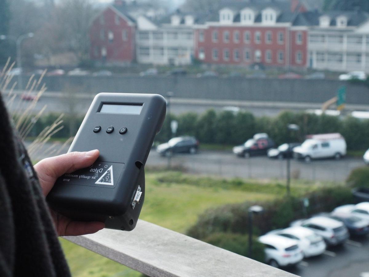 一个学生手里拿着空气质量测量仪，俯瞰着道路和建筑物