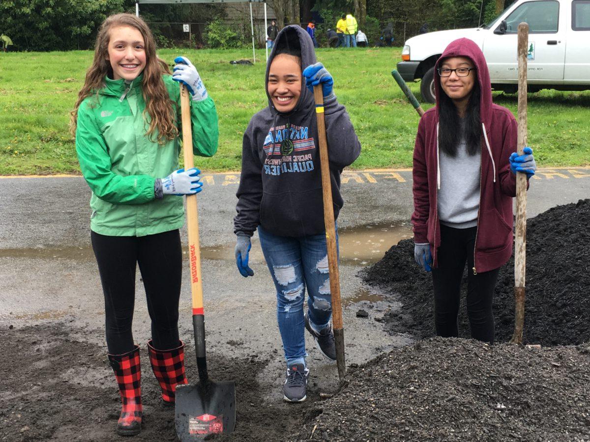 3 girls smile at the camera as they hold shovels