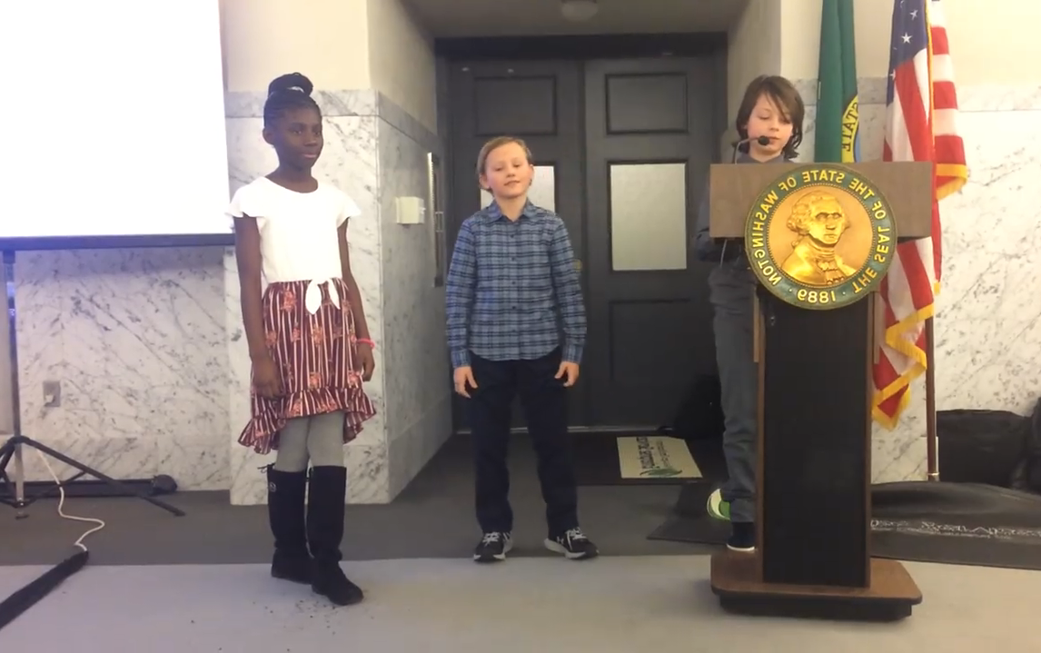 Three students on stage at the state Capitol in Olympia presenting their anti-idling campaign. 